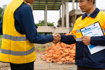 Two male architects, wearing hard hats and safety vests, discuss construction design while holding hands. They collaborate , focusing on the house structure, iron framework, brickwork, and roofing.