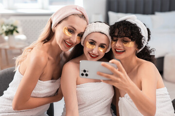 Wall Mural - Happy friends with eye patches taking selfie indoors. Spa party