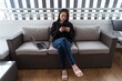 © ADDICTIVE STOCK CORE - Young woman using smartphone on cozy couch