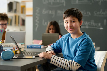 Portrait of teen boy looking at camera in school during computer class for children copy space