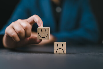 Wall Mural - hand holding smiley happy face on wooden cube and unhappy sad emotion on the floor. world mental hea