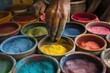 © Татьяна Евдокимова - Close up of an artisan's hand taking yellow pigment from a ceramic bowl, surrounded by other colorful powder pigments