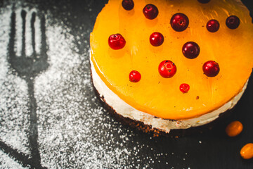 Dessert or cake made from autumn berries, sea buckthorn and lingonberries on cottage cheese cream and chocolate base. Bright yellow, afflicted with red berries on a black background.