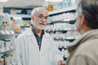 © lenblr - Senior male pharmacist wearing a lab coat talking with a customer about medication in a pharmacy
