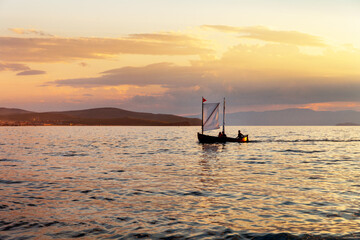 Wall Mural - Sunset landscape with silhouette of pleasure sailboat with tourists in distance. Siberian Baikal Lake in sunset light. Sunset over Small Sea on beach of Olkhon Island in Khuzhir . Natural background