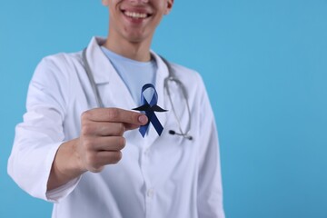 Sticker - Prostate cancer awareness. Doctor holding blue ribbon with fake mustache on color background, selective focus. Space for text