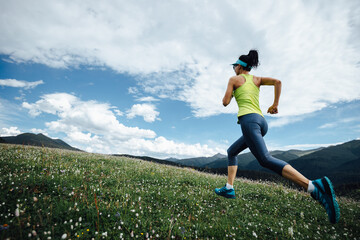 Wall Mural - Fitness woman runner running at flowering grassland mountain top