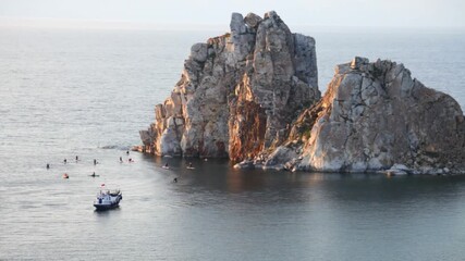 Wall Mural - Baikal Lake in summer. Video of a group of tourists riding sup boards at the famous Shamanka rock - Olkhon Island attractions at sunset. Summer activity