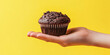 © Oleksandr - Hand elegantly holding a chocolate muffin against a bright yellow backdrop