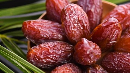 Poster - Dates fruit. Date fruits with palm tree leaf, in a wooden bowl, on black background. Medjool dates close up. Slow motion. 