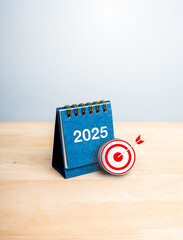 Wall Mural - Happy new year 2025 vertical banner. red 3d target icon with 2025 number on blue small desk calendar cover standing on wood table isolated on white background. Business goal and success concept.