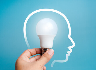 Poster - Creative idea, innovation, knowledge, idea and inspiration concept. Glowing bright white creative light bulb, holding by hand, inside human head outline graphic on blue background, minimal style.