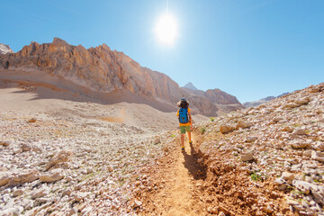 Wall Mural - summer camp. boy with a backpack. a boy with a backpack walks along a path against the background of mountains. travel and hiking. traveling with children to the mountains.