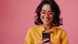 © Ajay - Cheerful young woman using smartphone on pink background.