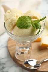 Wall Mural - Scoops of melon sorbet with mint in glass dessert bowl, fresh fruit and spoon on light marble table, closeup