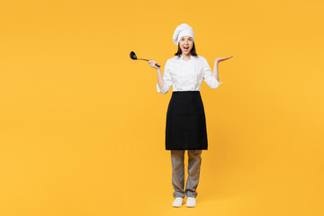 Wall Mural - Full body young chef cook baker woman wear white shirt apron uniform toque chefs hat hold in hand soup black ladle dipper spread hand isolated on plain yellow background studio. Cooking food concept.