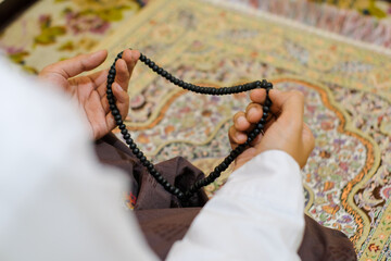 Close up Rear view shot of a hand man holding prayer beads, set against a colorful, patterned carpet. The photo captures a moment of reflection and spirituality. Ideal for content related to religion.