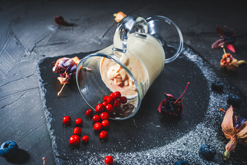 Wall Mural - Panna cotta in a transparent glass lying on a black mica board with lingonberries, blueberries and dried flowers. Original presentation, food design. Photo for menu, copyspace