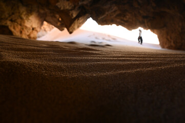 Young woman hiking in the background of a red natural rock cave in Algarve Portugal by the atlantic sea.