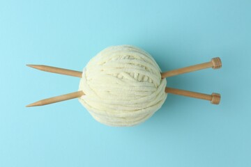 Poster - Ball of plush yarn with knitting needles on light blue background, top view