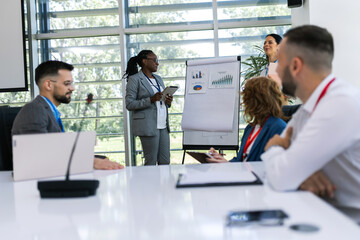 Two businesswoman talking on a meeting in an office with other colleagues. Showing graphics, diagrams and statistics.