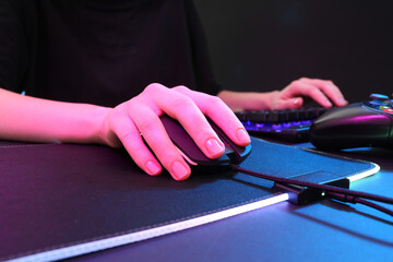 Wall Mural - Gamer using modern wired computer mouse in neon lights at dark table, closeup