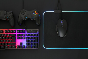 Wall Mural - Computer mouse, RGB keyboard and game controllers on black background, flat lay