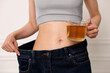 © New Africa - Weight loss concept. Woman with cup of diet tea and big pants near white wall, closeup