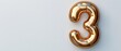 © Mikus - A gold balloon, shaped like the number three, on a white surface with a shadow casting the figure three