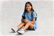 © Gonzalo - Happy young girl sitting on the floor, holding smartphone in hands and looking away