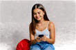 © Gonzalo - Happy young girl sitting on the floor, holding smartphone in hands and looking away