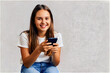 © Gonzalo - Happy young girl sitting on the floor, holding smartphone in hands and looking away