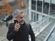 © vefimov - Professional man in coat and backpack walking on city stairs while talking on cell phone, smiling for camera.