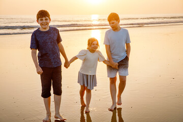 Three children, happy siblings on ocean beach at sunset. happy family, two school boys and one little preschool girl. Brothers and sister having fun, Spain, Costa del Sol