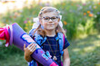 © Irina Schmidt - little girl with glasses and a blue backpack, dressed in a navy uniform, holds a colorful school cone called Schultuete and backpack. Happy child smiling, ready for her first day of school