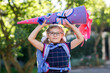 © Irina Schmidt - little girl with glasses and a blue backpack, dressed in a navy uniform, holds a colorful school cone called Schultuete and backpack. Happy child smiling, ready for her first day of school
