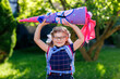 © Irina Schmidt - little girl with glasses and a blue backpack, dressed in a navy uniform, holds a colorful school cone called Schultuete and backpack. Happy child smiling, ready for her first day of school