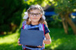 © Irina Schmidt - Happy little kid girl with eye glasses with backpack or satchel and big school bag on the first day of school. Healthy adorable child outdoors. Child holding chalks desk for first schoolday.