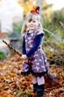 © Irina Schmidt - Portrait of Little Toddler Girl Dressed as a Witch Celebrating Halloween. Happy Child Outdoors, with an Orange Funny Hat and Holding a Witch Broom. Family Festival Season in October. Outdoor Activity.