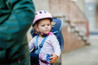 © Irina Schmidt - A smiling toddler girl wearing a pink helmet sits securely in a bicycle child seat, ready for a ride. The background is blurred, focusing on the child joyful expression