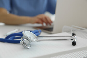 Wall Mural - Doctor at white table in hospital, focus on medical stethoscope