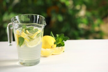 Canvas Print - Refreshing lemonade with mint in jug on light table against blurred green background. Space for text