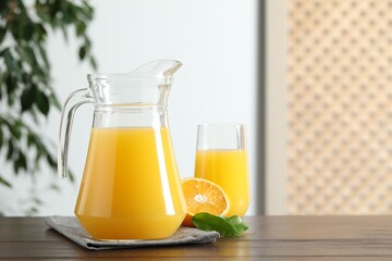 Wall Mural - Tasty orange juice in jug, glass and citrus fruit on wooden table. Space for text