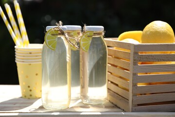 Wall Mural - Refreshing lemonade in bottles, fresh fruits, paper cups and straws on wooden table outdoors