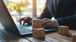 © Jodie - A man is typing on a laptop with three wooden blocks on the table