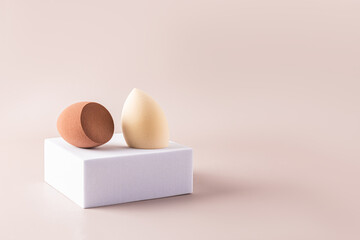 Beige and brown egg-shaped beauty sponge blenders on a square white catwalk and beige background. Front view. A sample of a makeup tool. A copy space.