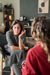 © Mediaphotos - Woman discussing personal issues while therapist listens attentively in cozy room with bookshelves and decor in background