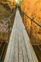 Wall Mural - a suspension bridge over the river on an autumn day