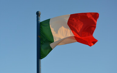 Bandera italiana: verde, blanca y roja; movida por el  viento al atardecer.