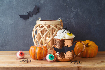 Wall Mural - Halloween holiday concept with coffee cup, marshmallow, pumpkin and lantern on wooden table over dark background